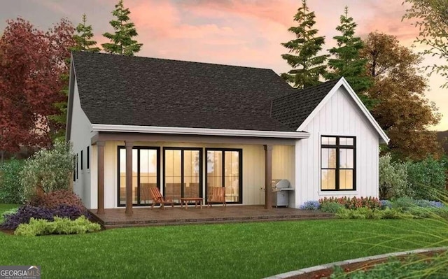 back of house with a patio area, a lawn, and roof with shingles