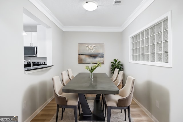 dining room featuring ornamental molding, a textured ceiling, and light wood-type flooring