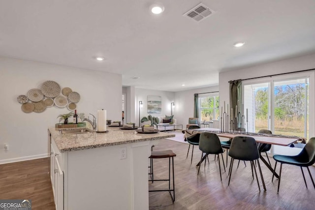 kitchen featuring a breakfast bar, sink, white cabinetry, light stone counters, and dark hardwood / wood-style floors