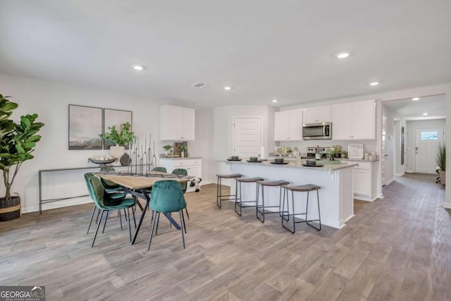 kitchen featuring light hardwood / wood-style floors, an island with sink, white cabinets, and appliances with stainless steel finishes