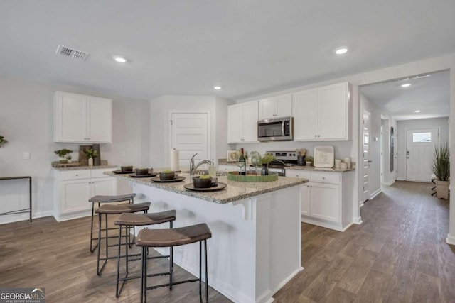 kitchen with stainless steel appliances, a breakfast bar area, a center island with sink, and white cabinets