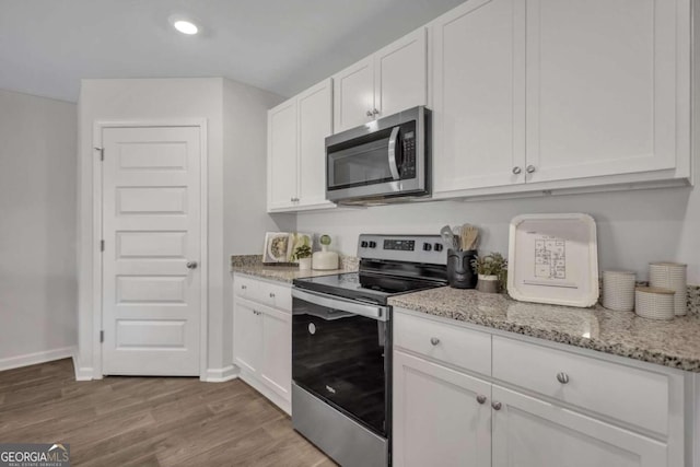 kitchen with light stone countertops, stainless steel appliances, white cabinets, and light wood-type flooring