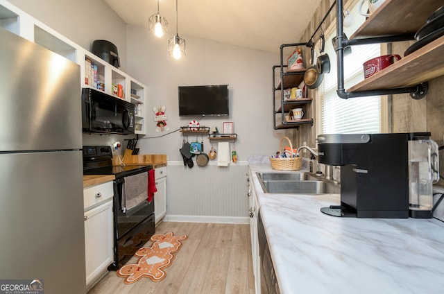 kitchen with light hardwood / wood-style floors, pendant lighting, black appliances, sink, and white cabinetry