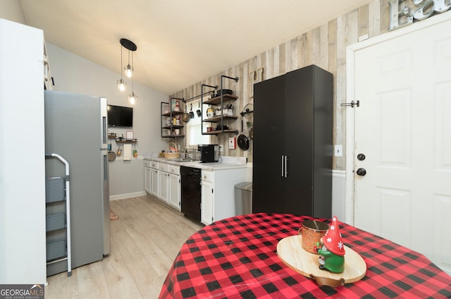 kitchen with lofted ceiling, black dishwasher, wood walls, stainless steel refrigerator, and white cabinetry