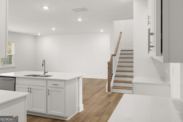 kitchen with light wood-type flooring, stainless steel dishwasher, sink, a center island with sink, and white cabinets