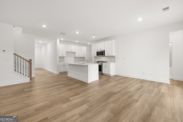 kitchen featuring light wood-type flooring, stainless steel appliances, sink, white cabinets, and an island with sink