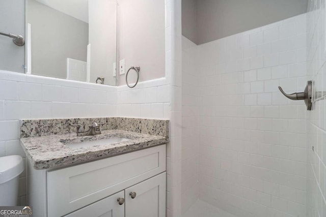 bathroom featuring vanity, toilet, tile walls, and a tile shower