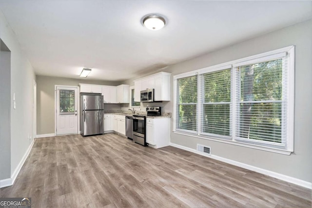 kitchen with light stone countertops, sink, light hardwood / wood-style floors, stainless steel appliances, and white cabinets