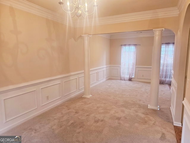 carpeted spare room featuring ornamental molding, decorative columns, and an inviting chandelier