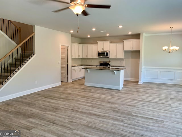 kitchen with stainless steel appliances, white cabinets, light hardwood / wood-style floors, an island with sink, and ceiling fan with notable chandelier