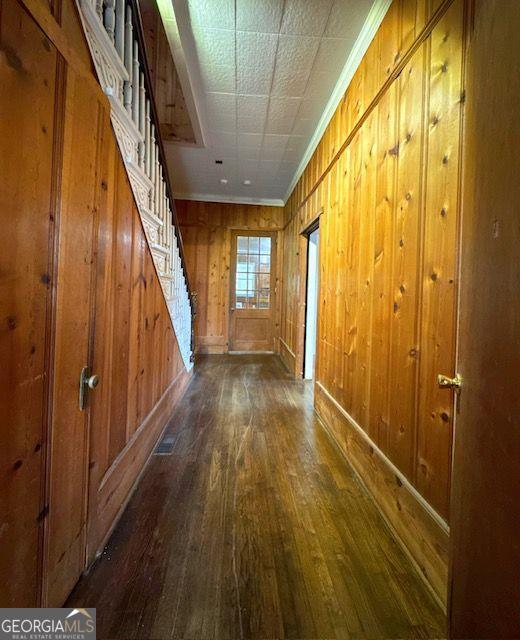 corridor with dark hardwood / wood-style flooring, crown molding, and wooden walls