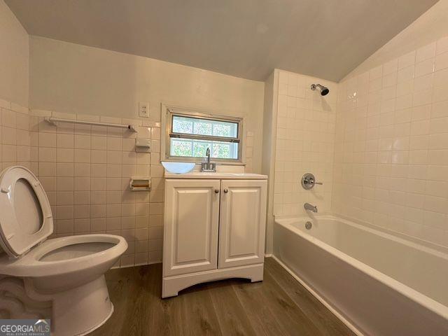 full bathroom with hardwood / wood-style floors, tiled shower / bath combo, tile walls, and lofted ceiling