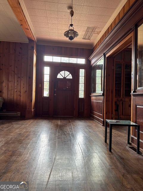 foyer entrance with dark hardwood / wood-style floors, wood walls, and crown molding