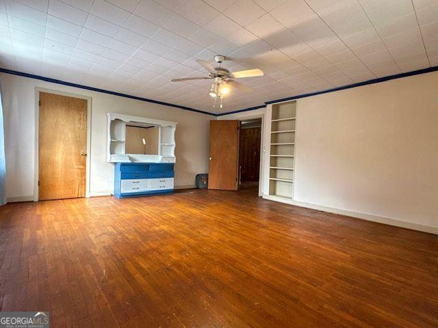 unfurnished living room featuring hardwood / wood-style floors, ceiling fan, built in features, and crown molding