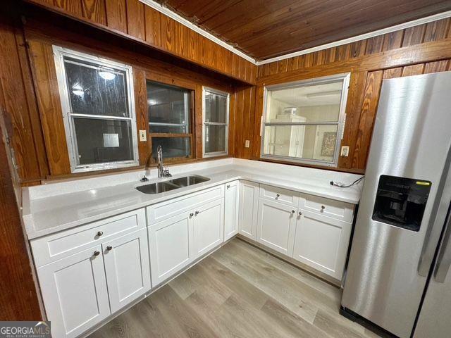 kitchen featuring sink, wooden ceiling, stainless steel refrigerator with ice dispenser, white cabinets, and light wood-type flooring