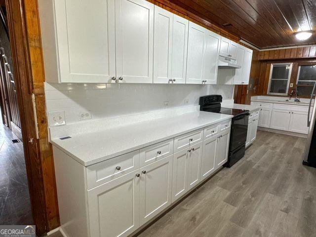 kitchen featuring sink, black electric range, white cabinetry, wood-type flooring, and wood ceiling