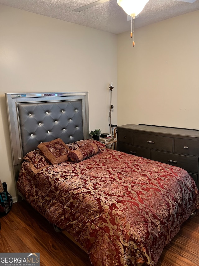 bedroom with ceiling fan, a textured ceiling, and dark hardwood / wood-style flooring