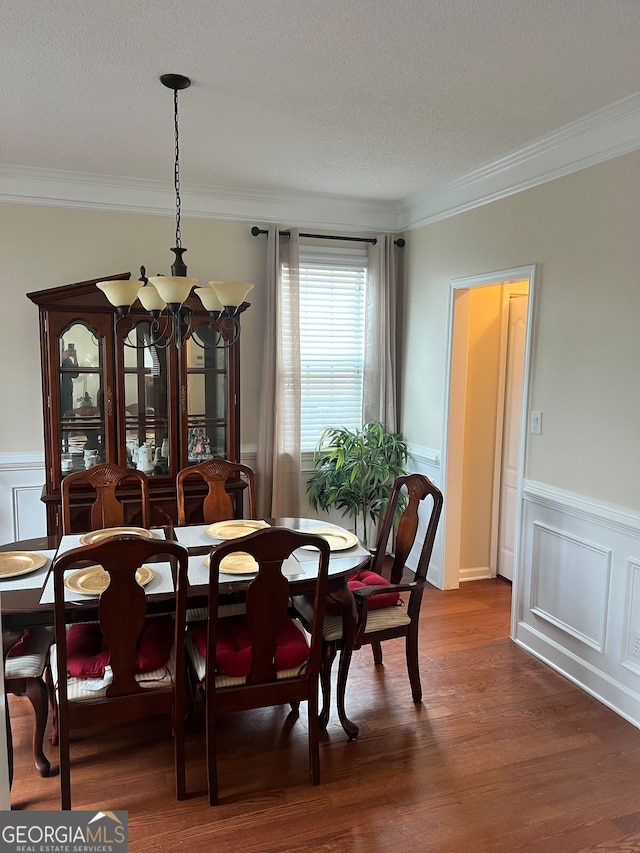 dining space with dark wood-type flooring, ornamental molding, a textured ceiling, and an inviting chandelier