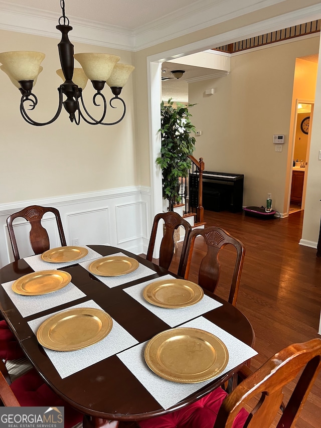 dining area with dark wood-type flooring, ornamental molding, and an inviting chandelier