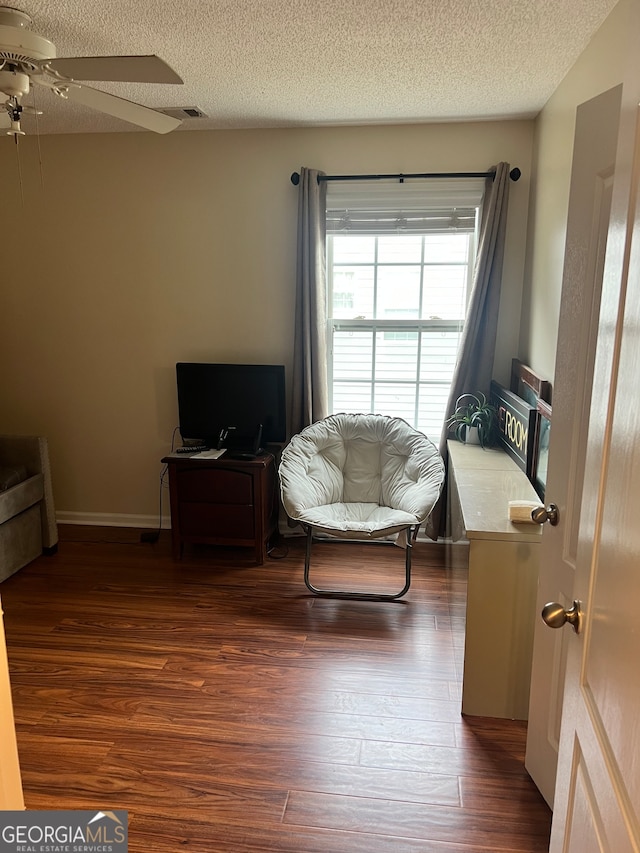 living area with a textured ceiling, ceiling fan, and dark hardwood / wood-style flooring