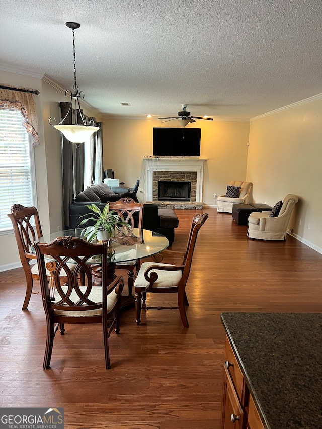 dining area with crown molding, a stone fireplace, a textured ceiling, and dark hardwood / wood-style flooring