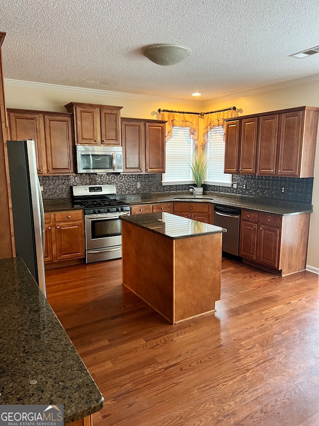 kitchen featuring dark wood-type flooring, stainless steel appliances, ornamental molding, and a kitchen island