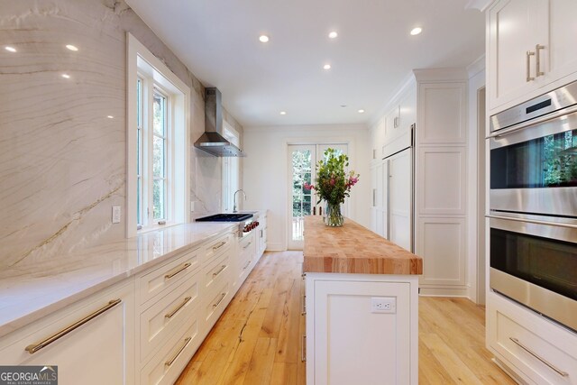 kitchen featuring white cabinetry, butcher block counters, wall chimney exhaust hood, and light hardwood / wood-style floors