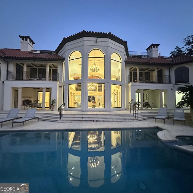 back of property featuring a balcony, a patio, and a pool with hot tub