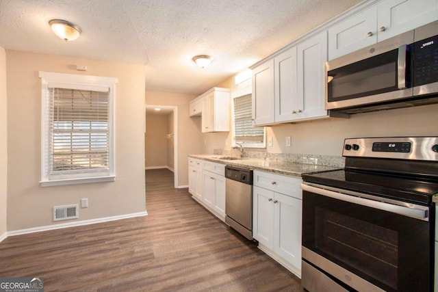 kitchen with dark wood-type flooring, light stone counters, appliances with stainless steel finishes, and white cabinets