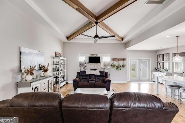 living room featuring french doors, beam ceiling, a brick fireplace, light wood-type flooring, and ceiling fan