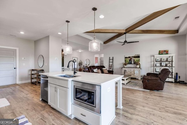 kitchen with a center island with sink, sink, pendant lighting, white cabinetry, and appliances with stainless steel finishes