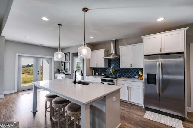 kitchen with wall chimney range hood, stainless steel appliances, pendant lighting, white cabinets, and a center island with sink