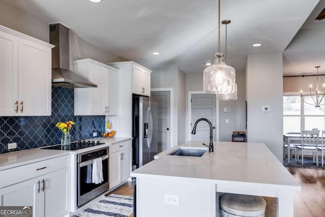 kitchen featuring wall chimney exhaust hood, appliances with stainless steel finishes, hanging light fixtures, and a center island with sink