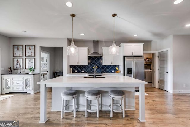 kitchen featuring wall chimney range hood, white cabinets, pendant lighting, light hardwood / wood-style floors, and stainless steel refrigerator with ice dispenser