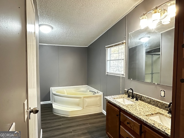 bathroom featuring lofted ceiling, hardwood / wood-style floors, a textured ceiling, a bath, and vanity