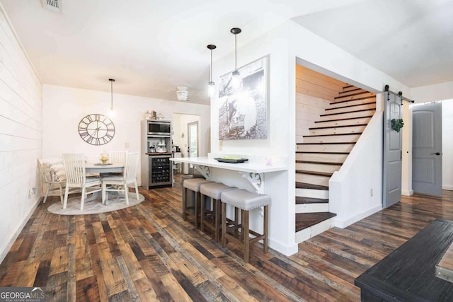 kitchen featuring a barn door, dark hardwood / wood-style flooring, kitchen peninsula, decorative light fixtures, and wine cooler