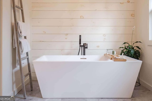 bathroom with concrete flooring, wooden walls, and a bathtub