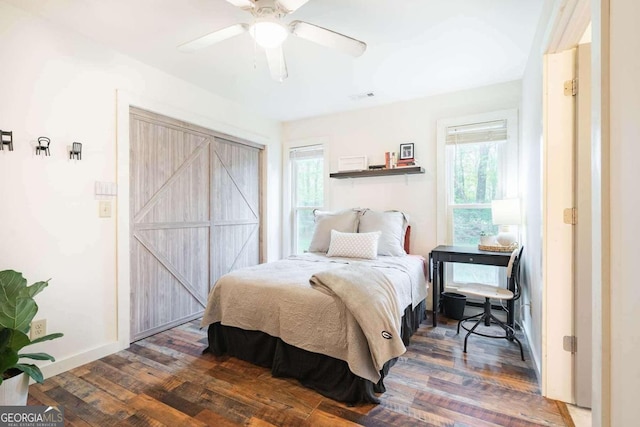 bedroom featuring ceiling fan, dark hardwood / wood-style floors, multiple windows, and a barn door