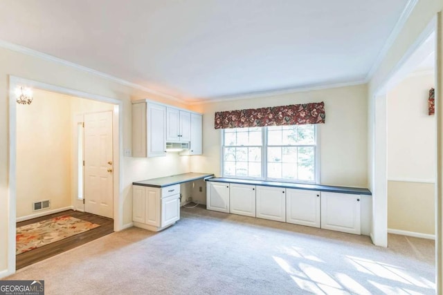 kitchen with crown molding, white cabinets, light colored carpet, and built in desk