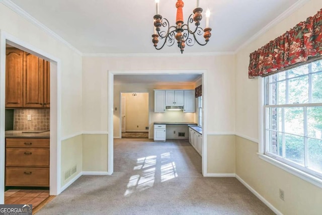 unfurnished dining area featuring crown molding, light carpet, an inviting chandelier, and plenty of natural light