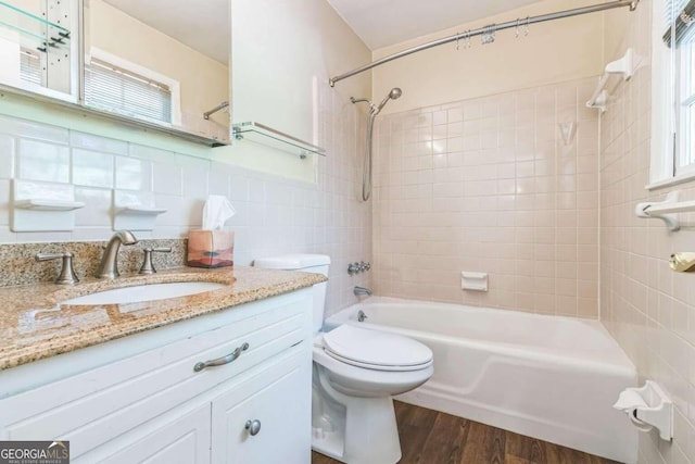 full bathroom with hardwood / wood-style flooring, tile walls, toilet, vanity, and tiled shower / bath combo