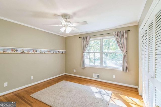 empty room featuring ornamental molding, light wood-type flooring, and ceiling fan