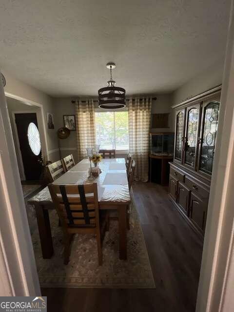 dining area featuring dark wood-type flooring, a textured ceiling, and an inviting chandelier