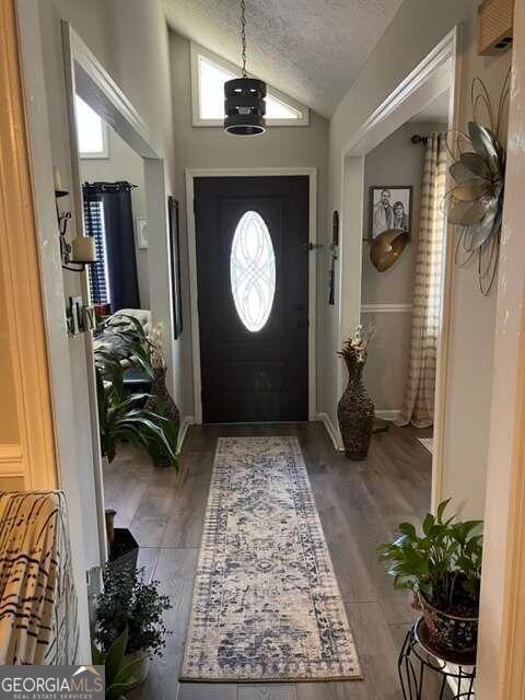 entryway featuring lofted ceiling, hardwood / wood-style floors, and a textured ceiling