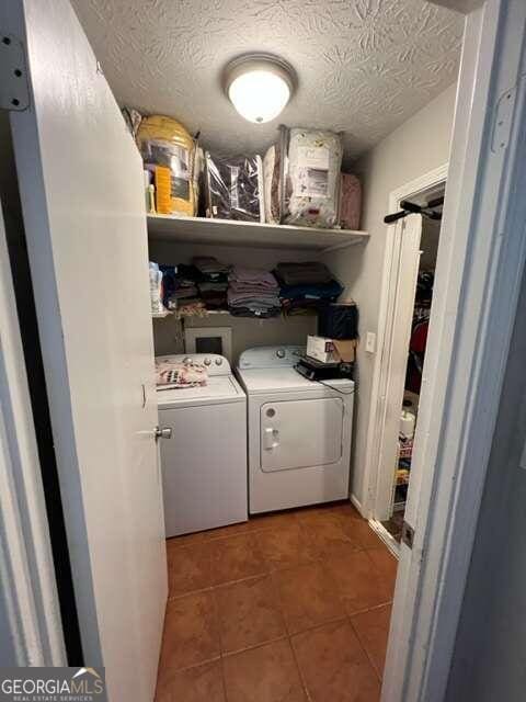 laundry room with a textured ceiling, washing machine and dryer, tile patterned flooring, and a barn door