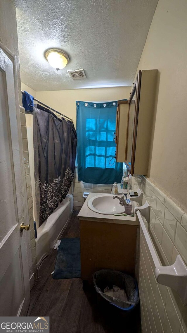 bathroom with a textured ceiling, hardwood / wood-style floors, tile walls, vanity, and shower / bathtub combination with curtain