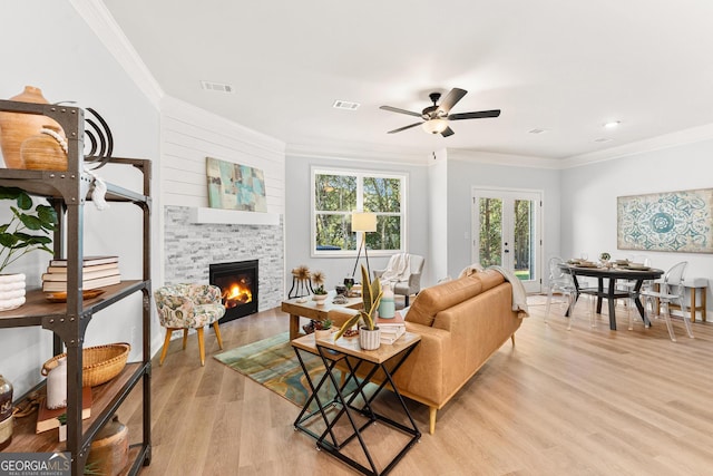 living room featuring ceiling fan, light wood-type flooring, a fireplace, crown molding, and french doors