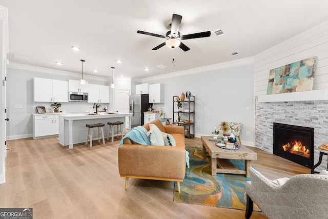 living room featuring a stone fireplace, ornamental molding, and light wood-type flooring