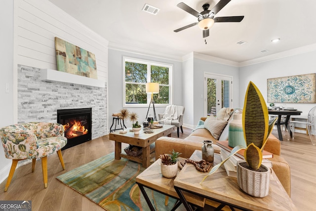 living room with ornamental molding, a stone fireplace, light wood-type flooring, and ceiling fan