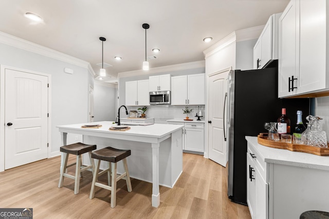 kitchen with hanging light fixtures, backsplash, an island with sink, white cabinetry, and light wood-type flooring